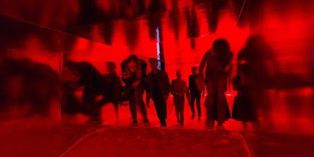 Spiegelnde Wände, rotes Licht, gewellter Boden: geduckt bewegen sich Besucher durch die Installation.