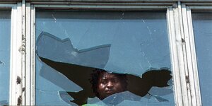 Ein schwarzer Mann schaut aus einem zerbrochenen Fenster