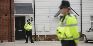 Zwei Polizisten in neongelben Westen stehen vor einem Haus