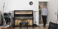 Ein Mann steht im Türrahmen eines Zimmers, in dem ein Klavier, ein Mikrophn und ein Laptop stehen