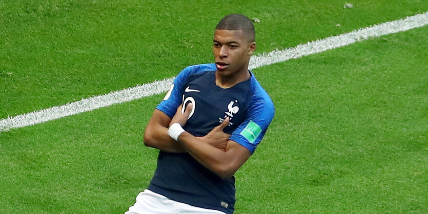 Kylian Mbappé feiert kniend und mit verschränkten Armen ein Tor auf dem Rasen