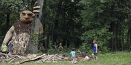 Parteienfinanzierung gegen Trolle: Eine übergroße Figur aus Holz lehnt an einem Baum, neben ihr Kinder und eine Frau
