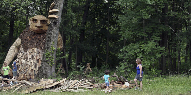 Parteienfinanzierung gegen Trolle: Eine übergroße Figur aus Holz lehnt an einem Baum, neben ihr Kinder und eine Frau