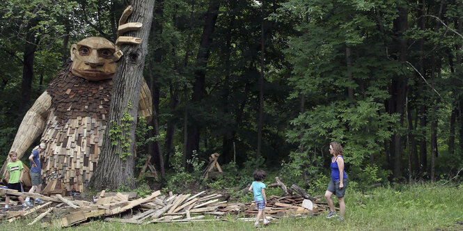 Parteienfinanzierung gegen Trolle: Eine übergroße Figur aus Holz lehnt an einem Baum, neben ihr Kinder und eine Frau