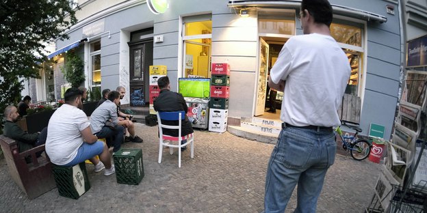 Menschen schauen Fußball vor einem Kiosk
