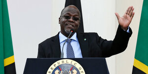Tansanias Präsident John Magufuli steht ein einem Rednerpult mit dem Logo von Kenia und hebt beim Reden die linke Hand
