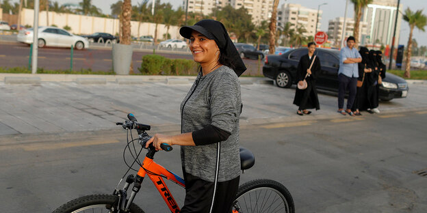 Saudi-Arabien: Frau geht mit ihrem Fahrrad an Palmen vorbei