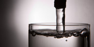 Aus einem Wasserhahn fließt Wasser in ein schon fast bis obenhin gefülltes Glas