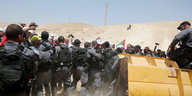 Ein Bulldozer, Sicherheitskräfte und Demonstrierende mit palästinensischen Flaggen, dazwischen Journalisten und Fotografen; im Hintergrund sandige Landschaft