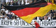 Jemand schwenkt die deutsche Fahne über einem Transparent: "Jerome sei unser Nachbar"