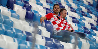 Zwei Kroatische Fans sitzen alleine in den Rängen eines Stadions.
