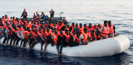 Geflüchtete sitzen mit Rettungswesten auf einem Schlauchboot