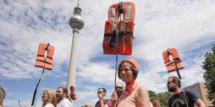 Menschen halten vor dem Fernsehturm Rettungswesten in die Höhe