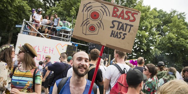 Ein junger Mann steht in einer Menschenmenge und trägt ein Schild mit der Aufschrift: „Bass statt Hass“