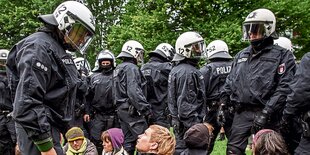 Menschen sitzten vor Polizisten, die in voller Montur sind