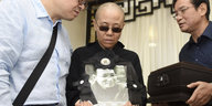 Liu Xia trägt eine Sonnenbrille und ein Bild von Liu Xiabo in der Hand