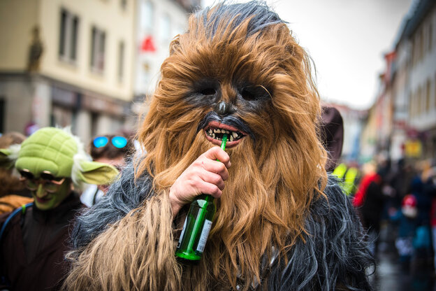 Eine Person, die als die haarige Star Wars-Figur verkleidet ist, trinkt mit einem Strohhalm aus einer Bierflasche.
