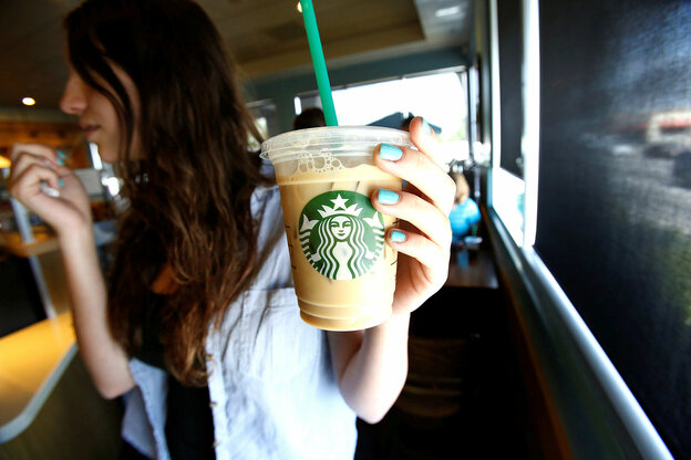Eine Frau mit grünen Fingernägeln hält in einer Starbucks-Filiale einen Becher mit Kaltgetränk und Strohhalm.