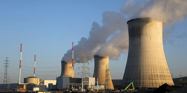 Drei Reaktoren eines AKWs vor einem blauen Himmel; es steigt Rauch auf