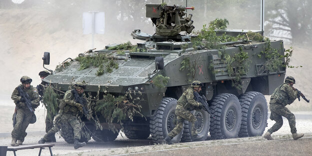 Nato-Soldaten laufen auf einem Truppenübungsplatz um einen Panzer