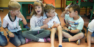 Vier Kinder sitzen nebeneinander, spielen und kommunizieren über Gebärdensprache