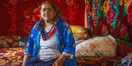 Eine ältere Frau sitzt auf einem Bett in einem bunt dekorierten Raum