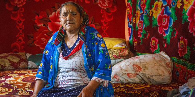 Eine ältere Frau sitzt auf einem Bett in einem bunt dekorierten Raum