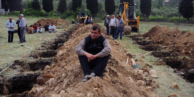 Ein Mann sitzt zwischen offenen Löchern, die als Gräber für Unfallopfer gegraben wurden