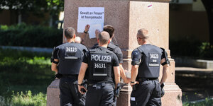 Polizisten überkleben Schrift an einer Säule
