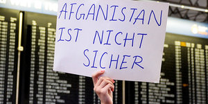Vor einer Anzeigewand am Flughafen wird ein Schild hochgehalten: „Afghanistan ist nicht sicher“