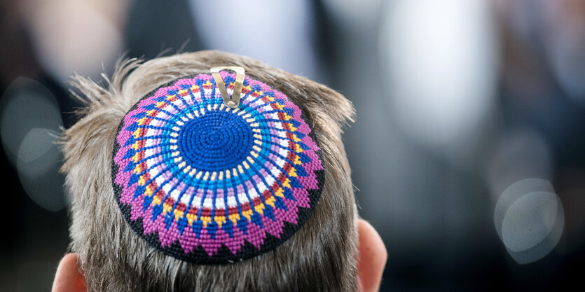 Ein Mann hält sich seine Kippa mit einem blauen Davidstern auf dem Kopf, daneben weitere Männer mit Kippot