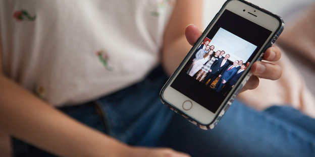 Eine Frau zeigt ein Bild auf dem Smartphone, auf dem eine Gruppe Menschen zu sehen sind
