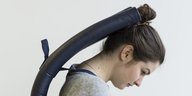 Eine Frau trägt eine Art futuristischen Rucksack, der ihren Kopf nach vorne beugt