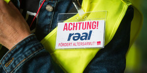 Eine Beschäftigte von Real trägt ein Schild, das vor Armut im Alter warnt