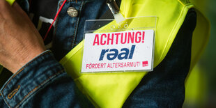 Eine Beschäftigte von Real trägt ein Schild, das vor Armut im Alter warnt