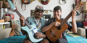 Die Musiker Arish Ahmad Khan und Saba Lou Khan sitzen mit Gitarren in den Händen auf einem Sofa