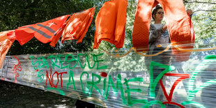 Eine Aktivistin der Gruppe "Seebrücke" hängt ein Transparent mit der Aufschrift "Sea Rescue is not a Crime" am Versammlungsort einer Demonstration auf.