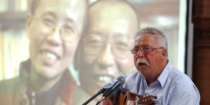 Gedenken für Liu Xiaobo in Berlin: Vorne ein Mann mit Gitarre, es ist Wolf Biermann, hinter ihm ein Foto von Liu Xia und Liu Xiaobo
