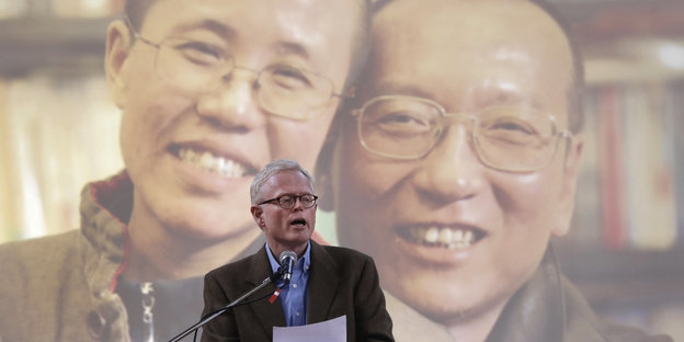Ian Johnson hält eine Rede für Liu Xiaobo - vorne ein Mann mit einem Zettel, hinten an die Wand projiziert ein Mann und eine Frau - Liu Xia und Liu Xiaobo