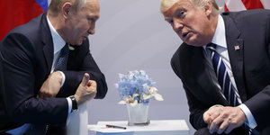 Wladimir Putin und Donald Trump lehnen sich über einen kleinen Tisch zueinander. Sie reden miteinander