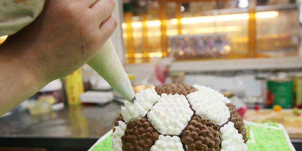 Ein Konditor verziert eine Torte, die wie ein Ball aussieht