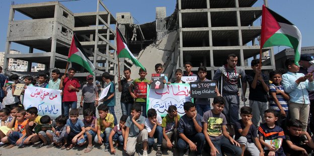 palästinensische Kinder demonstrieren vor zerschossenem Gebäude