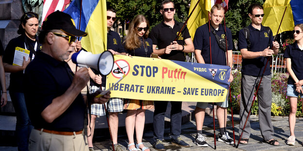 Demonstranten halten ein gelbes Transpi, auf dem Stop Putin steht