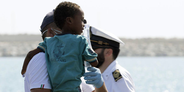 Ein Sanitäter hält ein Kind, das von der italienischen Küstenwache in Pozzallo, Sizilien, an Land gebracht wurde