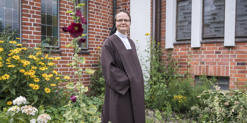 Maria Burger steht in einem Garten vor einem Gebäude aus roten Backsteinen.