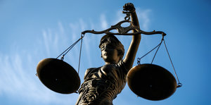 Die Statue einer Justizia mit Waagschale in der Hand vor blauem Himmel