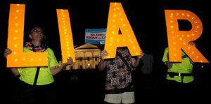 Demonstranten halten bei Nacht vier Leuchtbuchstaben in die Luft: LIAR