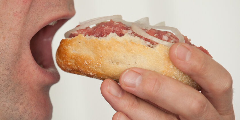 Ein Mann hält ein Mettbrötchen in der Hand und schiebt es sich in den Mund