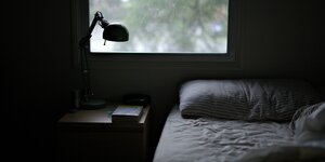 Ein Bett und ein Nachttisch mit Lampe vor einem Fenster.