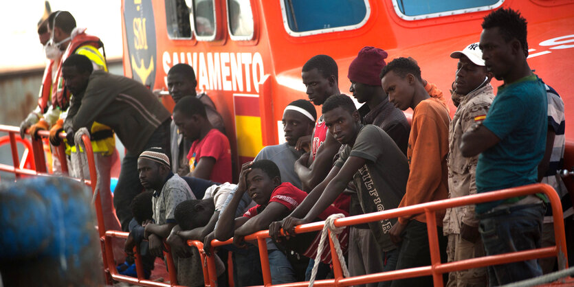 Menschen stehen an der Reling eines orangefarbenen Schiffes